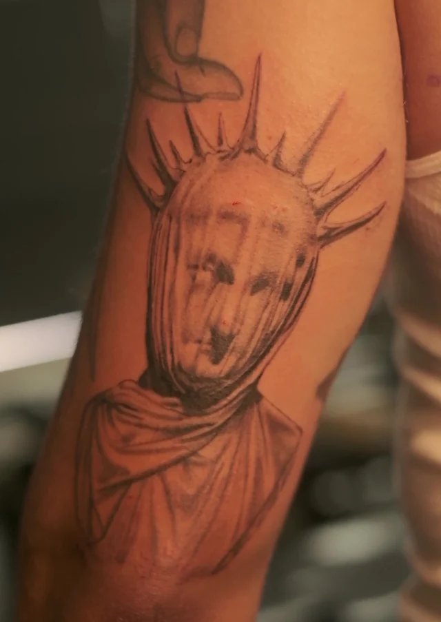 Black and grey crowned portrait tattoo on a forearm by Mason Hemphill
